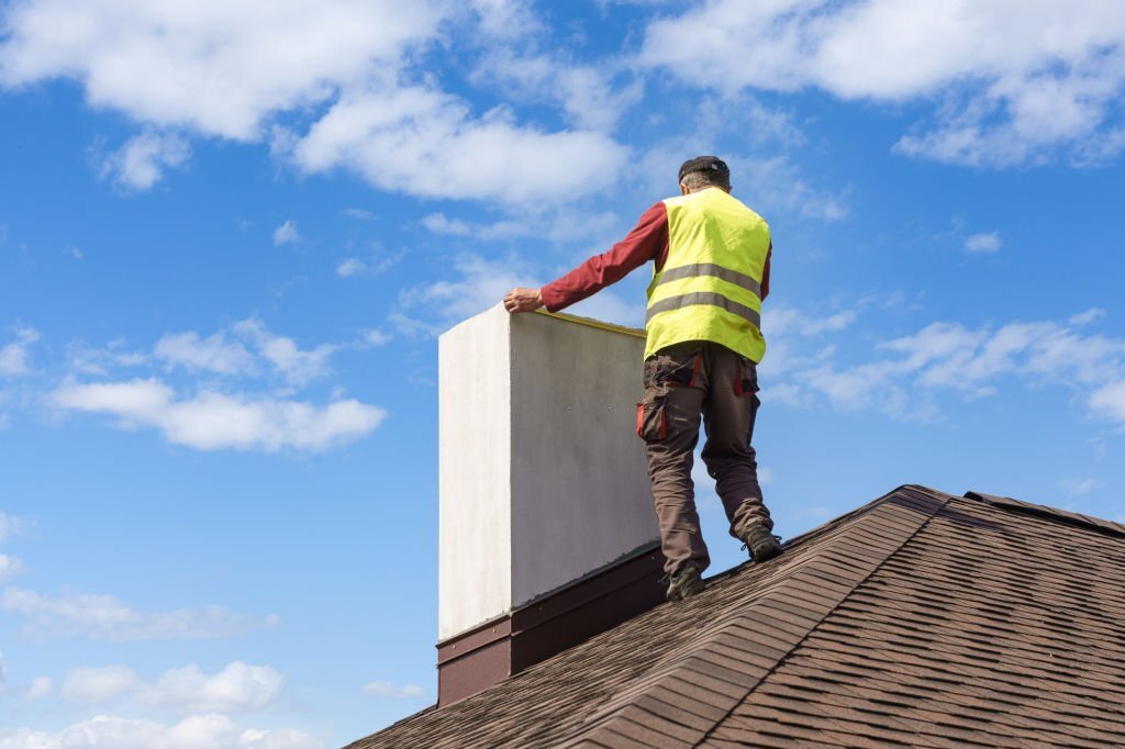 Professional workman standing roof top and measuring chimney of new house under construction against blue background