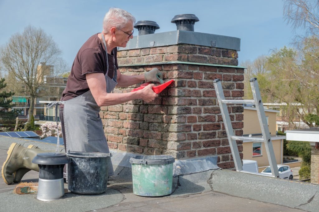 grey haired senior man grouts chimney on roof of house