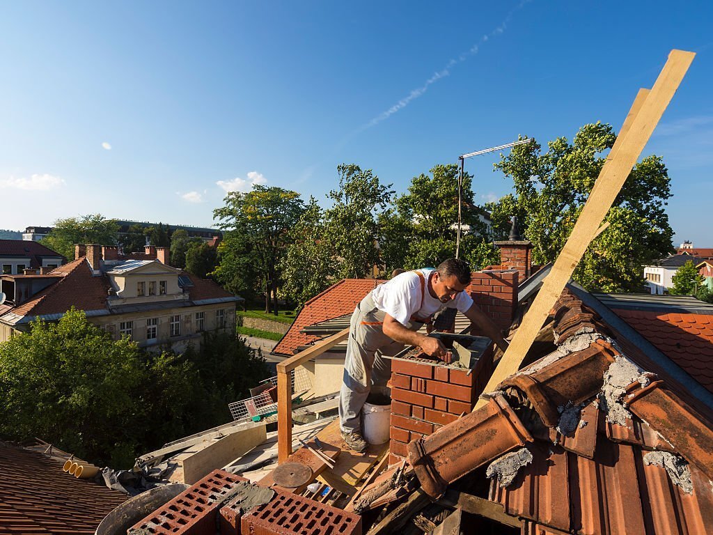 Partial renovation of the roof brick chimney of an old house in Ljubljana. Man is preparing mortar on chimney for new line of briks.